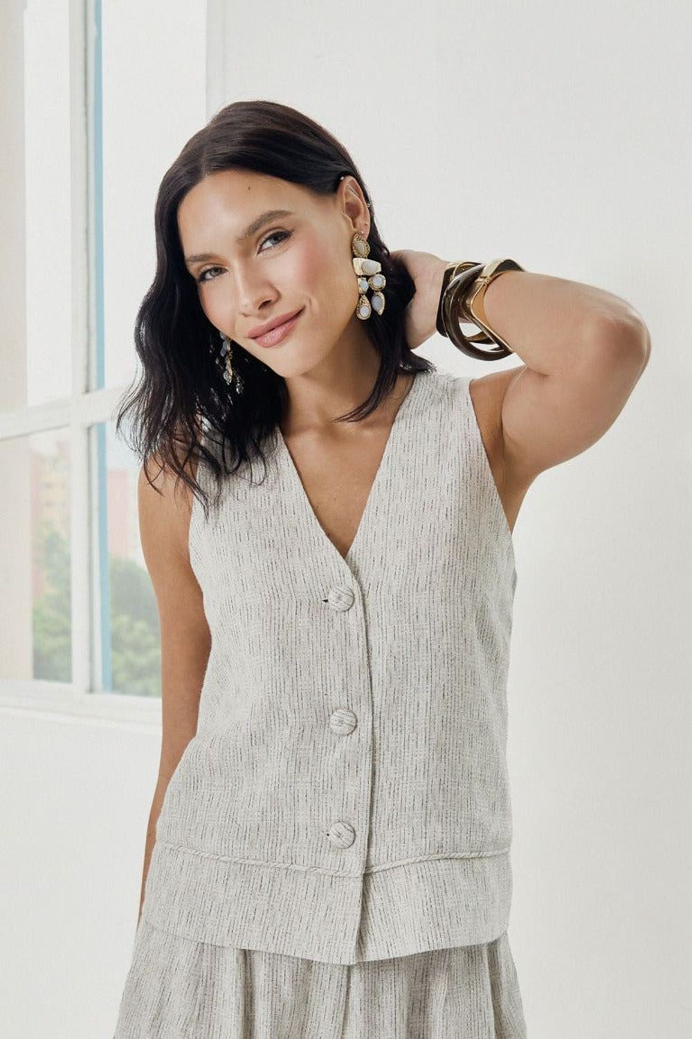 Blusa Alfaiataria Zoe Skenn bege com botões, vestida em modelo de cabelo castanho com brinco e pulseiras