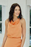 Blusa Skenn Decote Degage em laranja, com caimento drapeado no decote, vestida em modelo sorridente de lado
