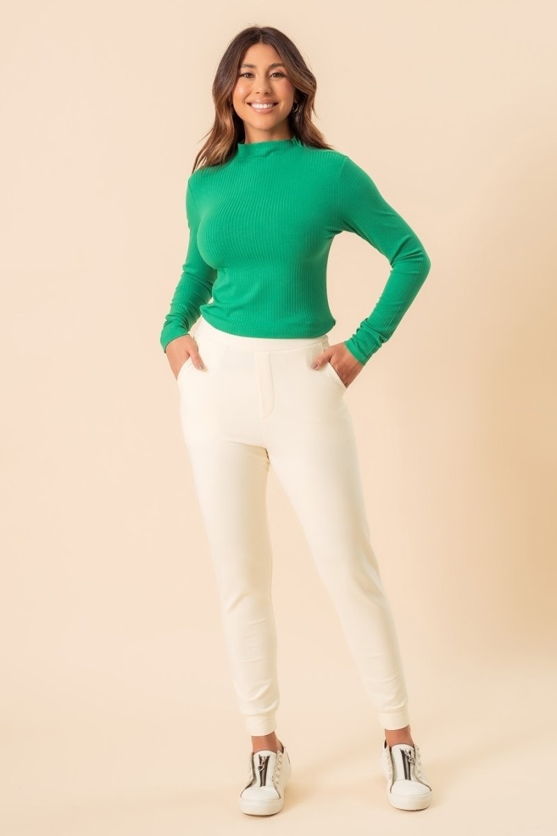 Blusa Coqueta manga longa gola alta canelada off-white, modelo sorridente de corpo inteiro com calça clara Imagem principal do produto