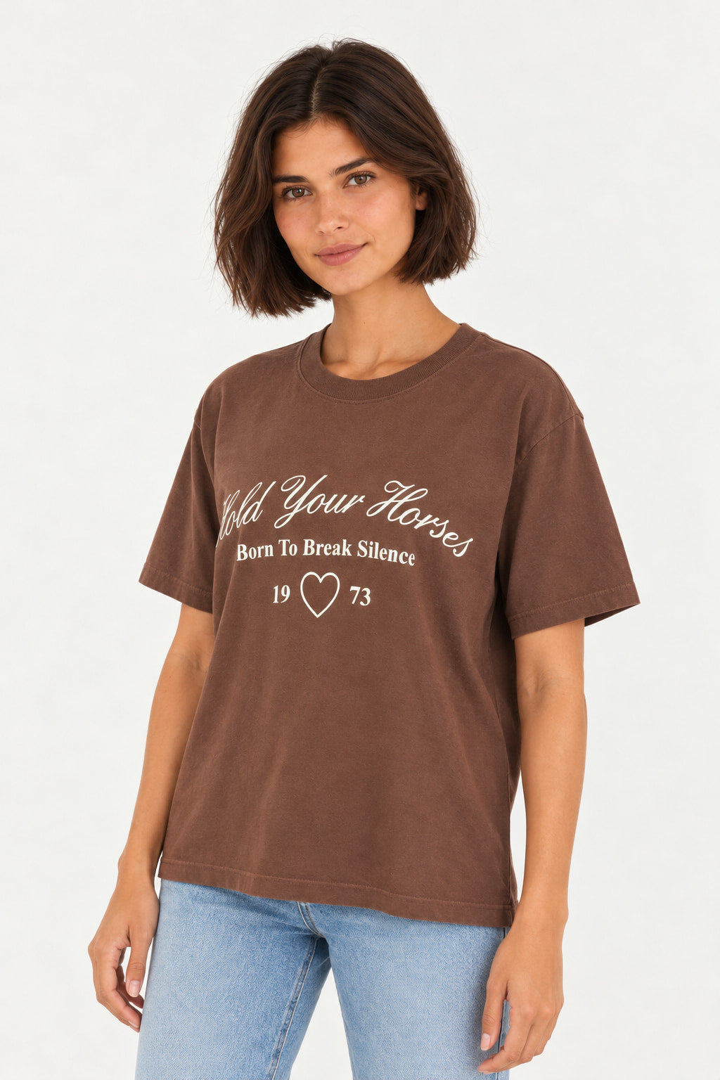 Marrom | Blusa T-Shirt Pasta Lerrux marrom com escrita Hold Your Horses em letra cursiva e coração branco, modelo com calça jeans