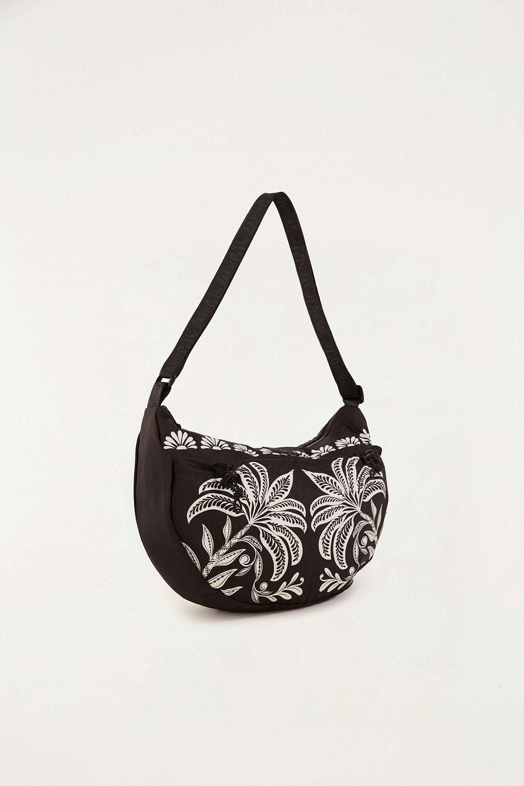 Bolsa Farm Banana G Coqueiro Sereno preta estampada com coqueiros brancos, vista em ângulo lateral com alça ajustável