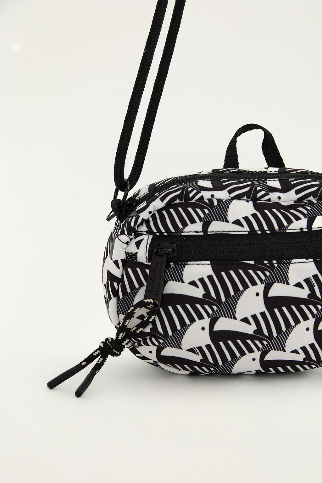 Detalhe do zíper e do cordão com pingente da bolsa Farm Chuchu Universitária Rolezin preta e branca