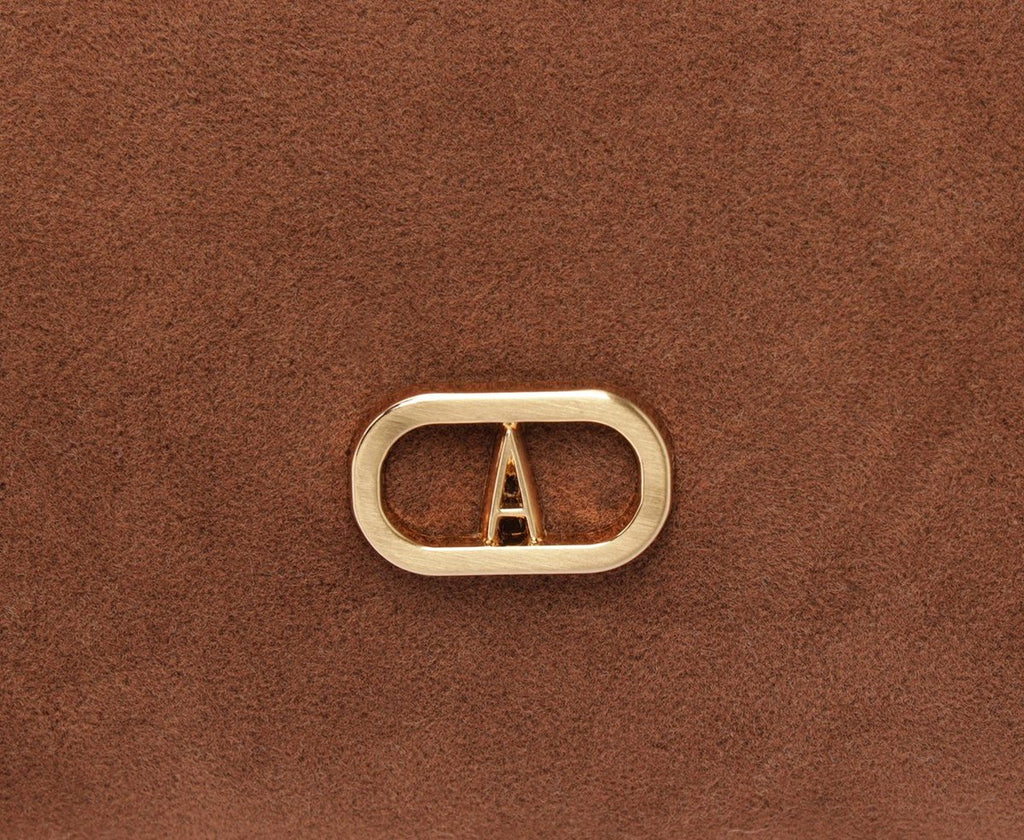 Detalhe do logo dourado em formato oval com letra A na bolsa Anacapri Tube marrom em camurça