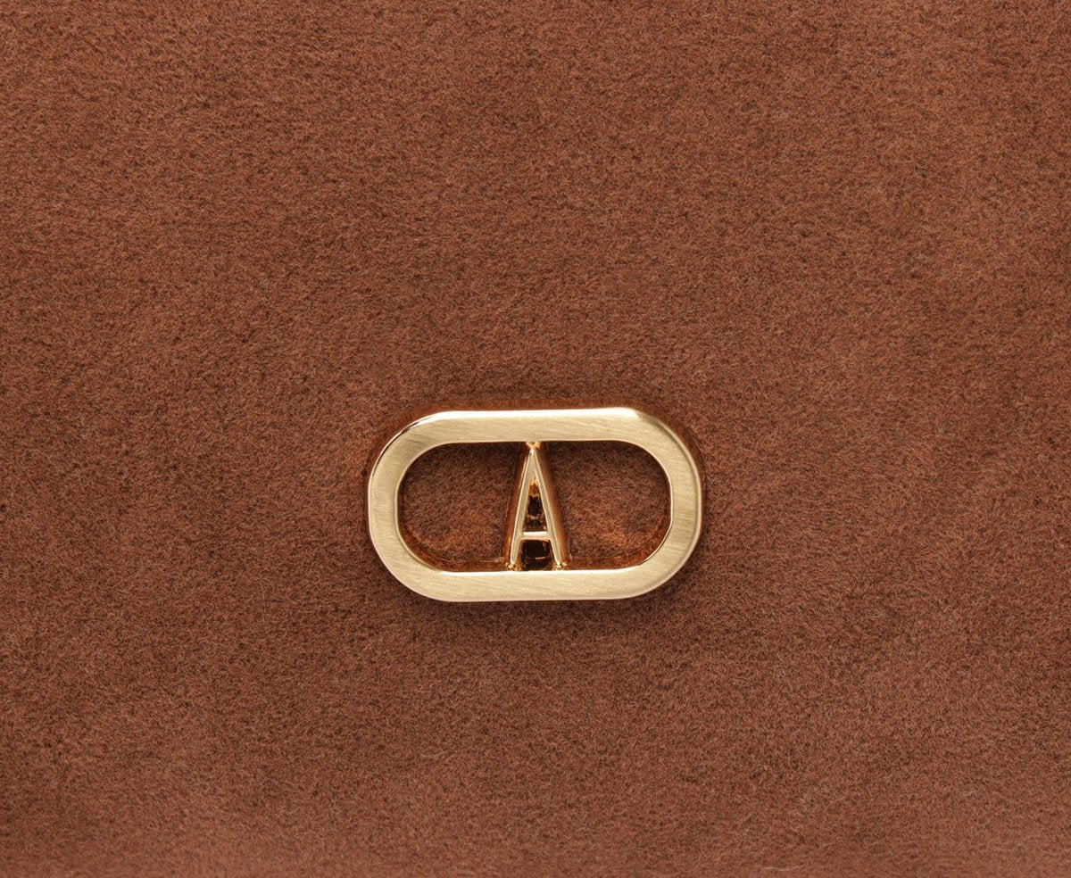 Detalhe do logo dourado em formato oval com letra A na bolsa Anacapri Tube marrom em camurça