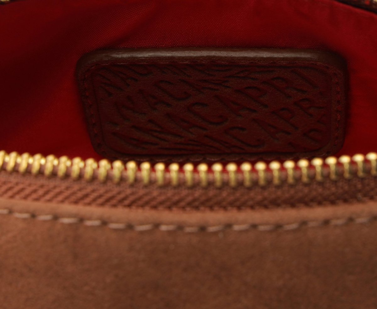 Detalhe do forro vermelho da bolsa Anacapri Tube marrom com etiqueta de couro gravada com a marca