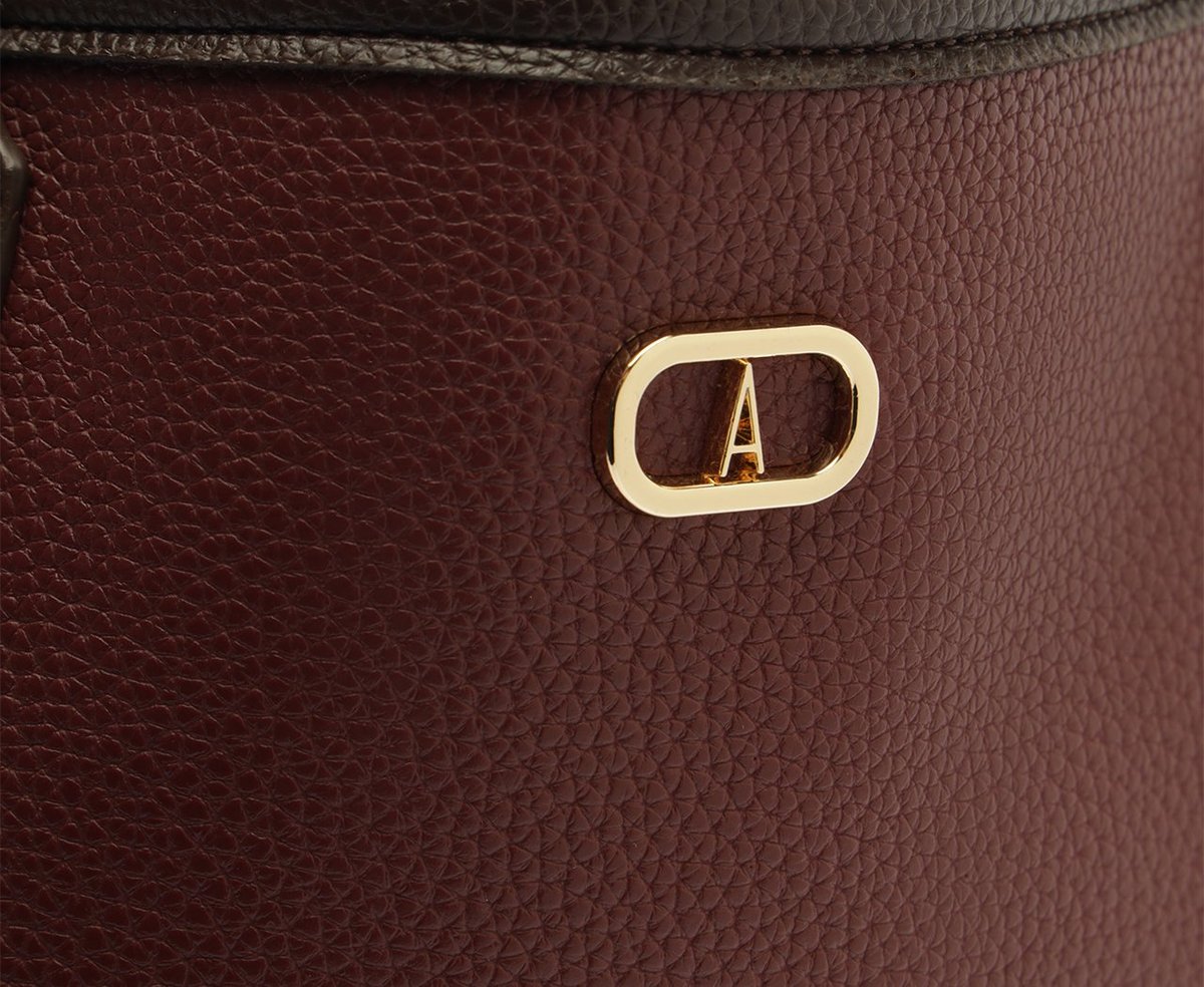 Detalhe do logotipo dourado Anacapri em bolsa marrom, sobre o couro granulado em tom vinho