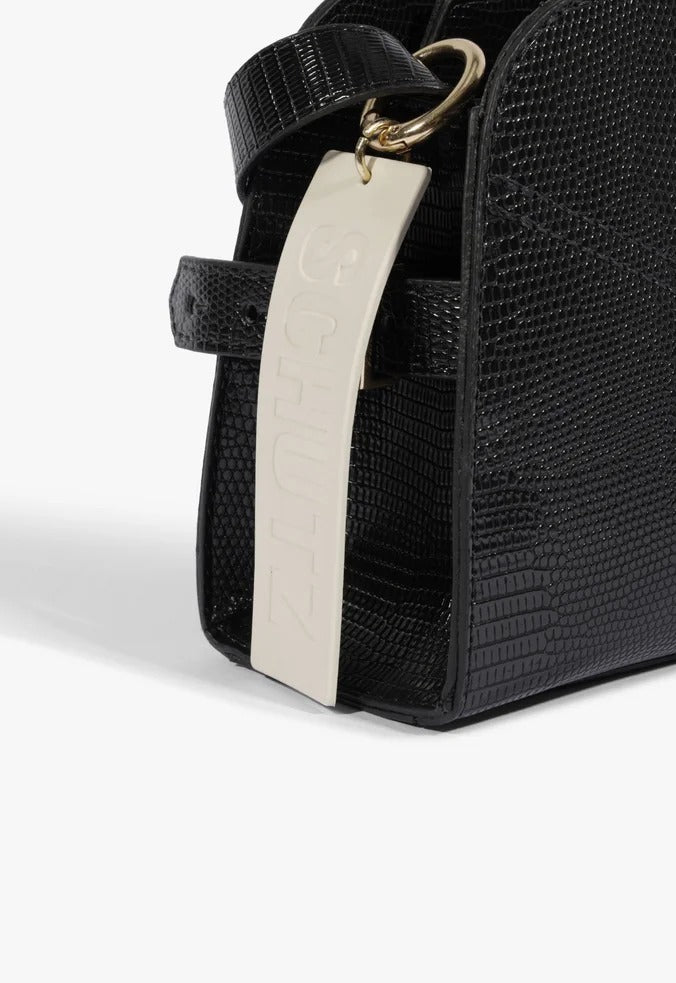 Detalhe da bolsa Schutz Hazel Pequena preta, com fivela dourada, alça e tag de marca creme em relevo