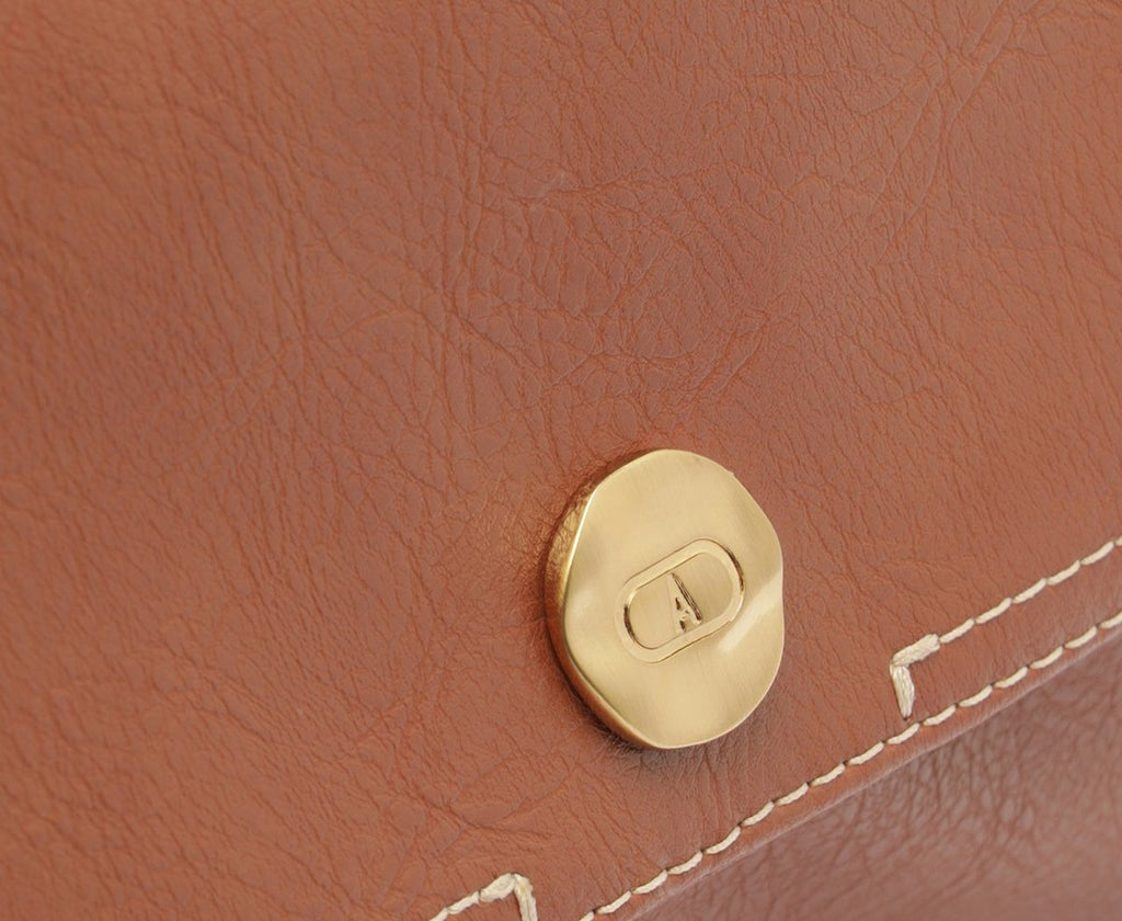 Detalhe do fecho dourado da bolsa Anacapri Rústica marrom caramelo sobre a aba