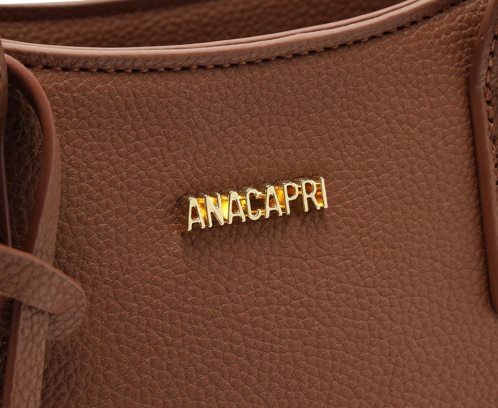 Detalhe da placa dourada com o nome Anacapri na bolsa Tote marrom, com textura granulada do material