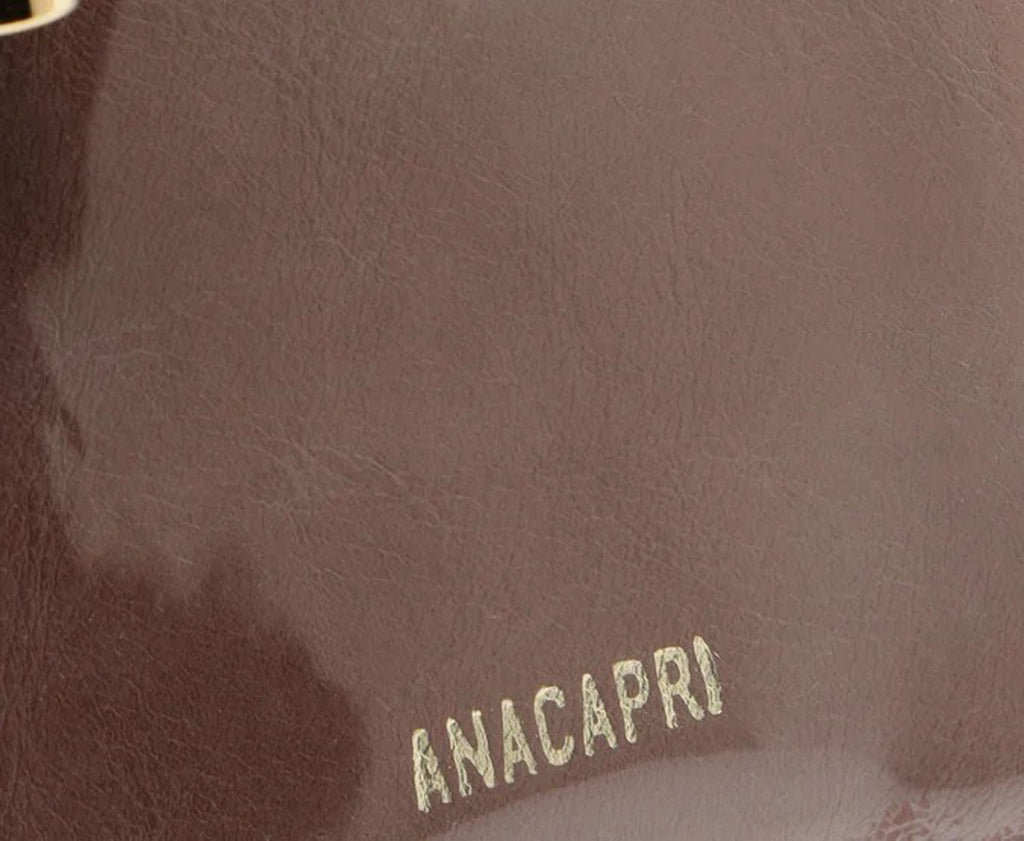 Detalhe da marca Anacapri em dourado gravada na etiqueta marrom da bolsa tote pequena preta