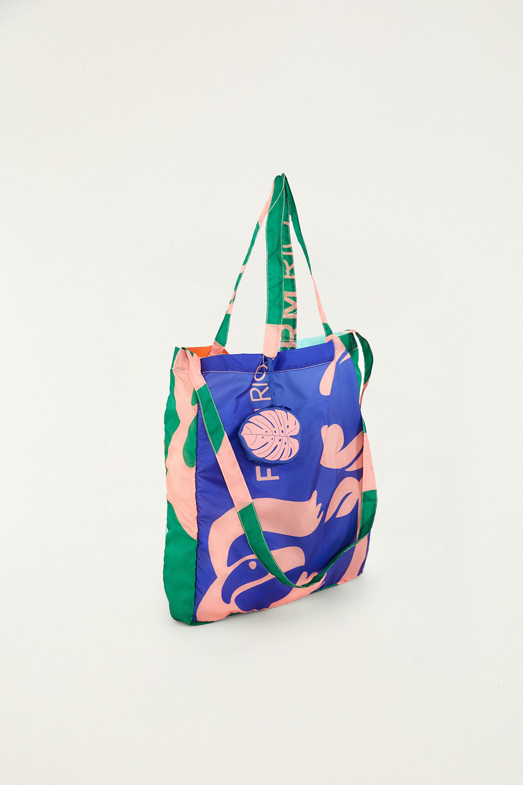 Bolsa Farm Me Leva Lisos Farm Etc estampada em azul e rosa vista de lado, com alças verdes e chaveiro de folha