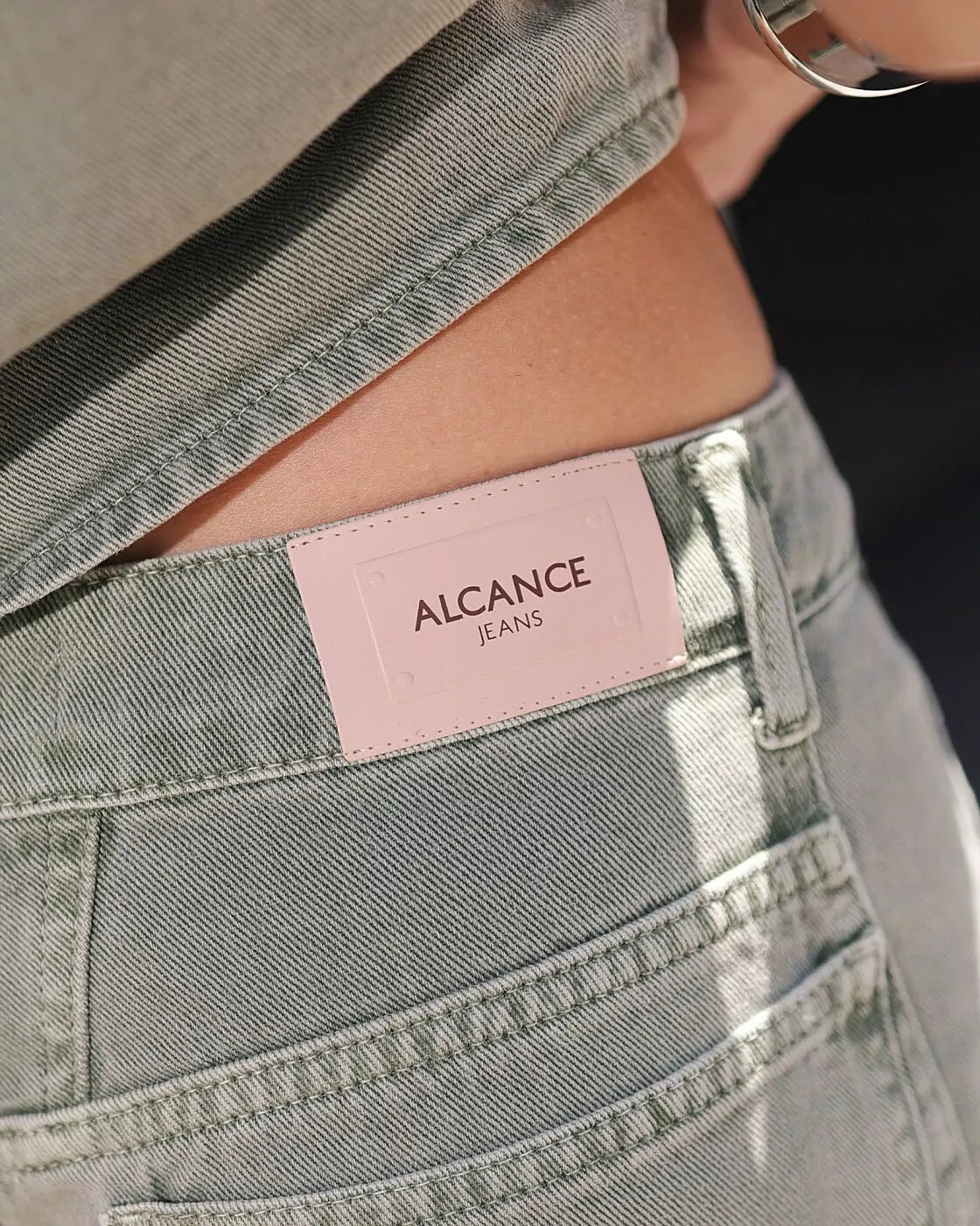 Calça Balloon Austin Alcance verde com etiqueta de couro rosa da marca Alcance Jeans no bolso traseiro