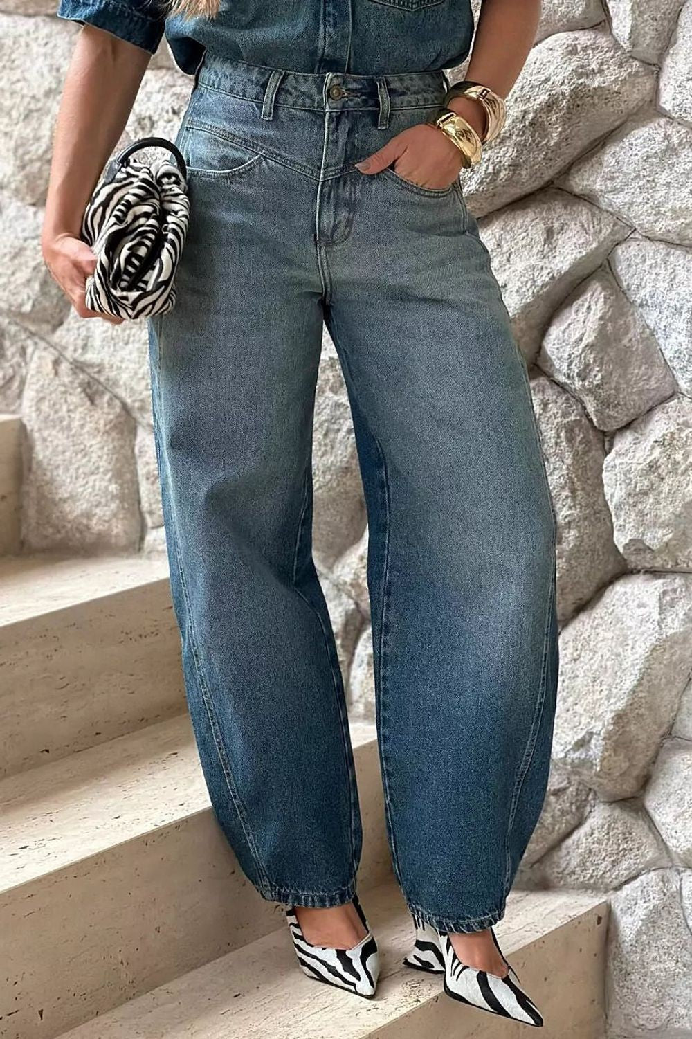 Calça jeans balloon Austin Alcance em azul médio, vestida na modelo com cinto, bolsa zebra e sapato de estampa animal