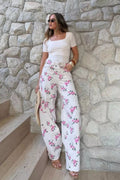 Calça Jeans Balloon Rose Flower Alcance em off white com estampa de rosas rosa, com modelo de top branco encostada em muro de