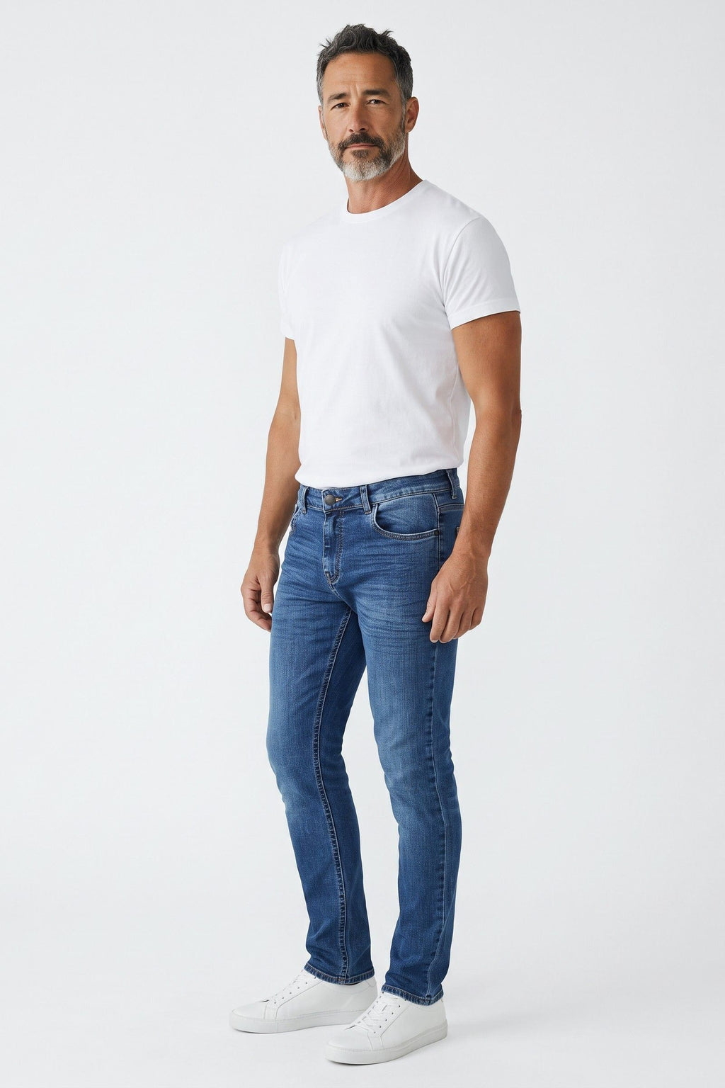 Calça jeans masculina slim Revanche em azul médio, vestida em modelo de camiseta branca e tênis branco, vista de corpo inteir