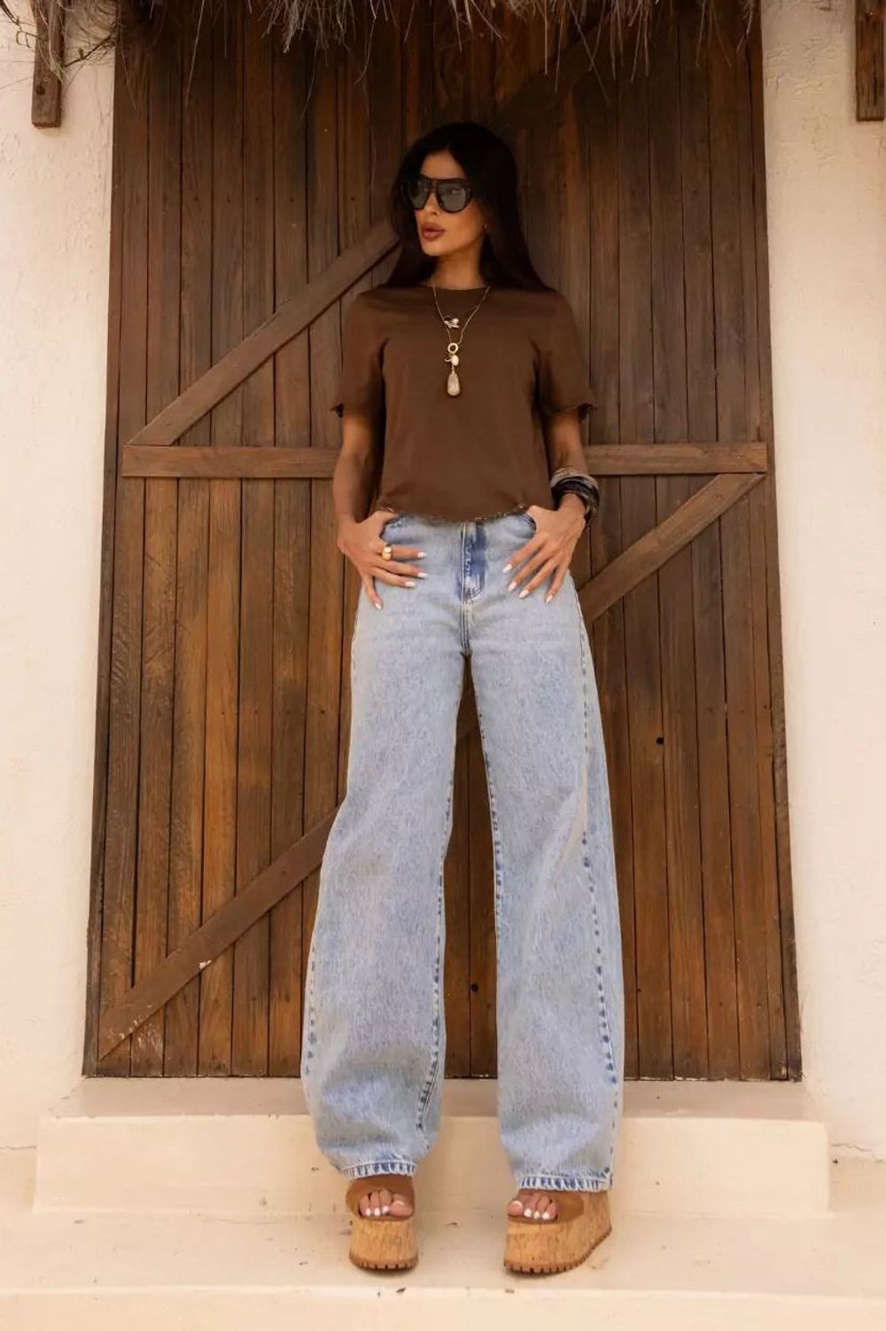 Calça Jeans New Baggy Alcance azul claro, vestida na modelo com camiseta marrom e sandália plataforma de cortiça Imagem principal do produto