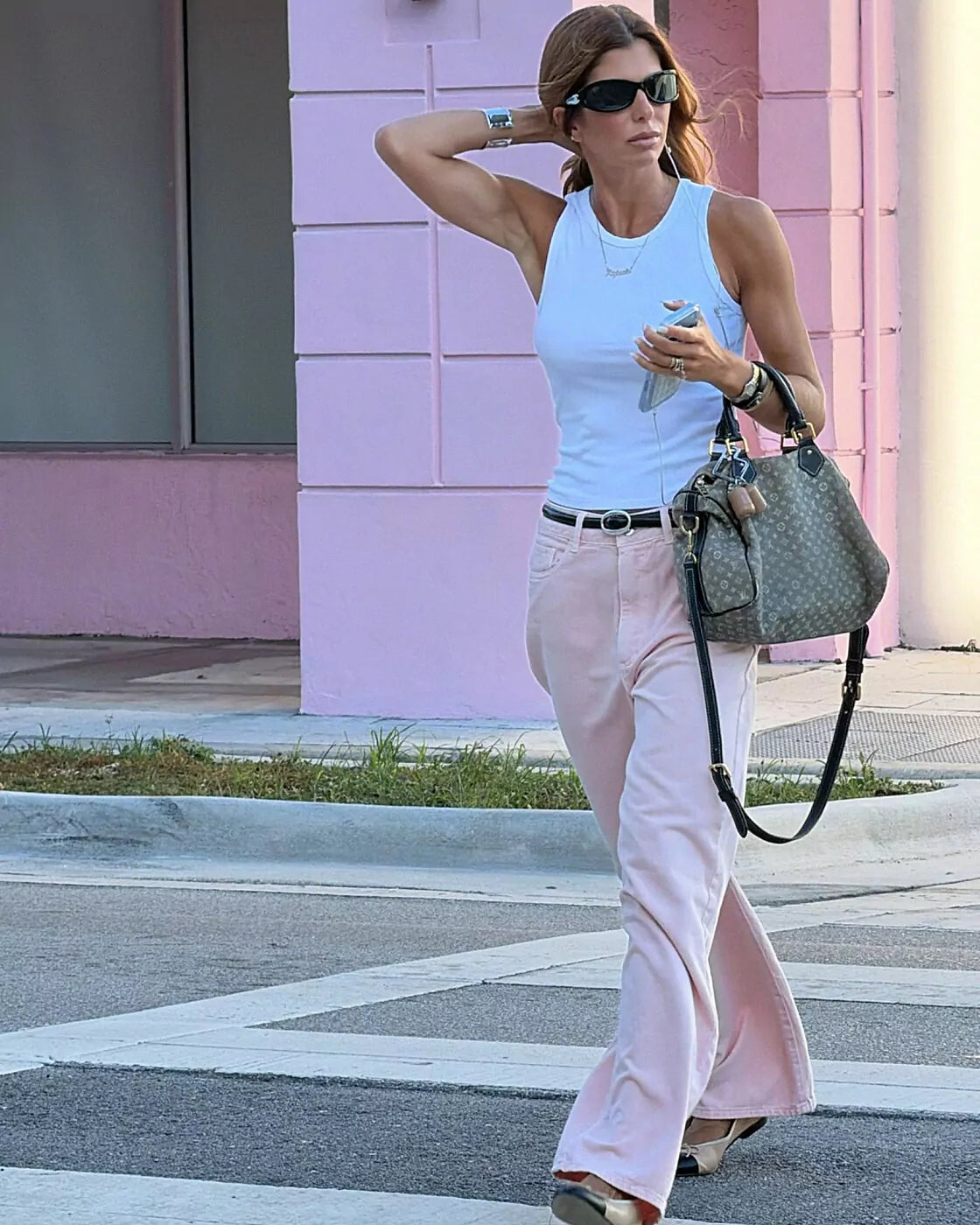 Calça Alcance New Baggy Botanic rosa com cinto preto caminhando na rua com regata branca e bolsa monograma