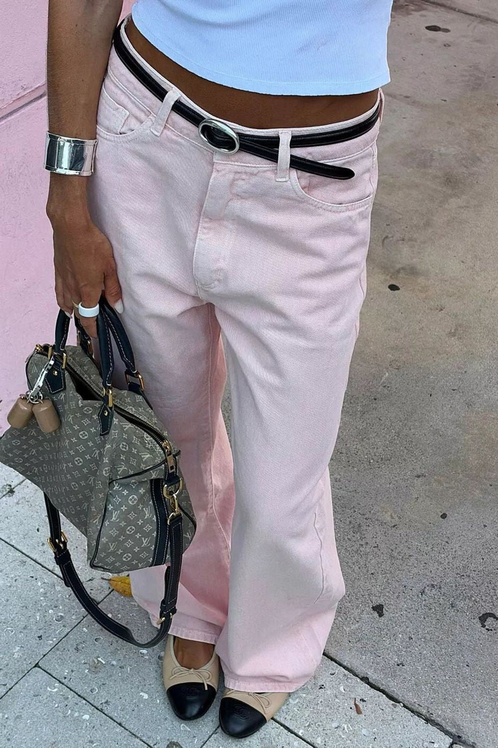 Calça Alcance New Baggy Botanic rosa com cinto preto, vestida na modelo com blusa branca cropped e bolsa