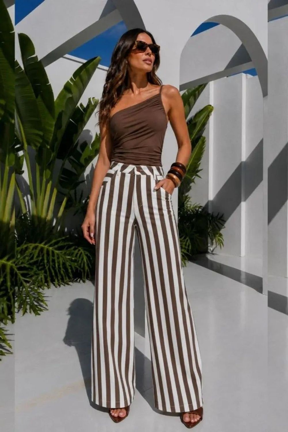 Calça sarja Skenn listra com modelo de pernas largas em marrom e branco, vestida em look com regata marrom