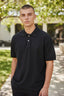 Camiseta Polo Masculina Revanche preta, com dois botões e bordado discreto no peito, vestida em modelo ao ar livre