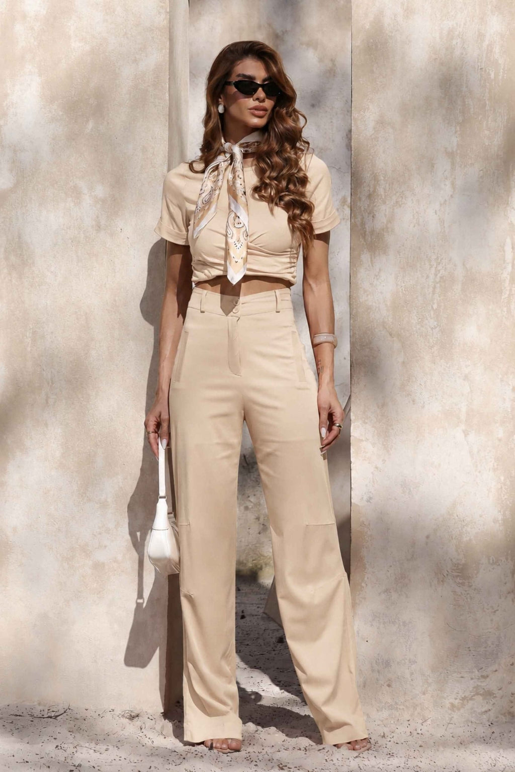 Conjunto Amicia pantalona cropped em bege com lenço estampado e bolsa branca em frente a parede clara