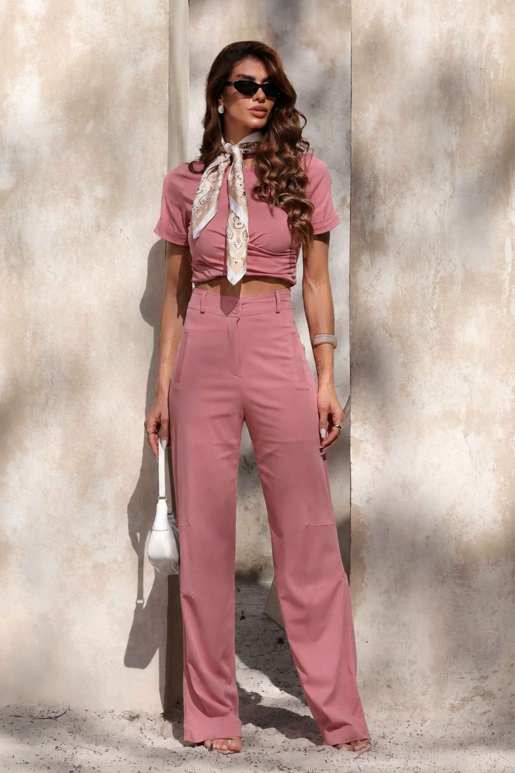 Conjunto Amicia pantalona cropped em rosa antigo com lenço estampado e bolsa branca em frente a parede clara