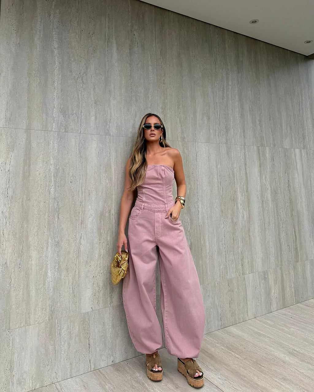 Macacão Aladim Cloud Alcance rosé de corpo tomara que caia e calça pantalona com bolsos, modelo de corpo inteiro encostada na