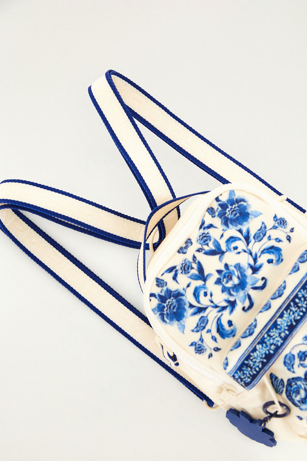 Mini Mochila Farm Borogodó Porcelain Farm Etc deitada, mostrando as alças listradas em azul e off-white e a estampa floral az