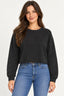 Preto | Blusa Moletom Cropped Alcance preta, de manga longa e gola redonda, vestida em modelo de cabelos castanhos com jeans azul