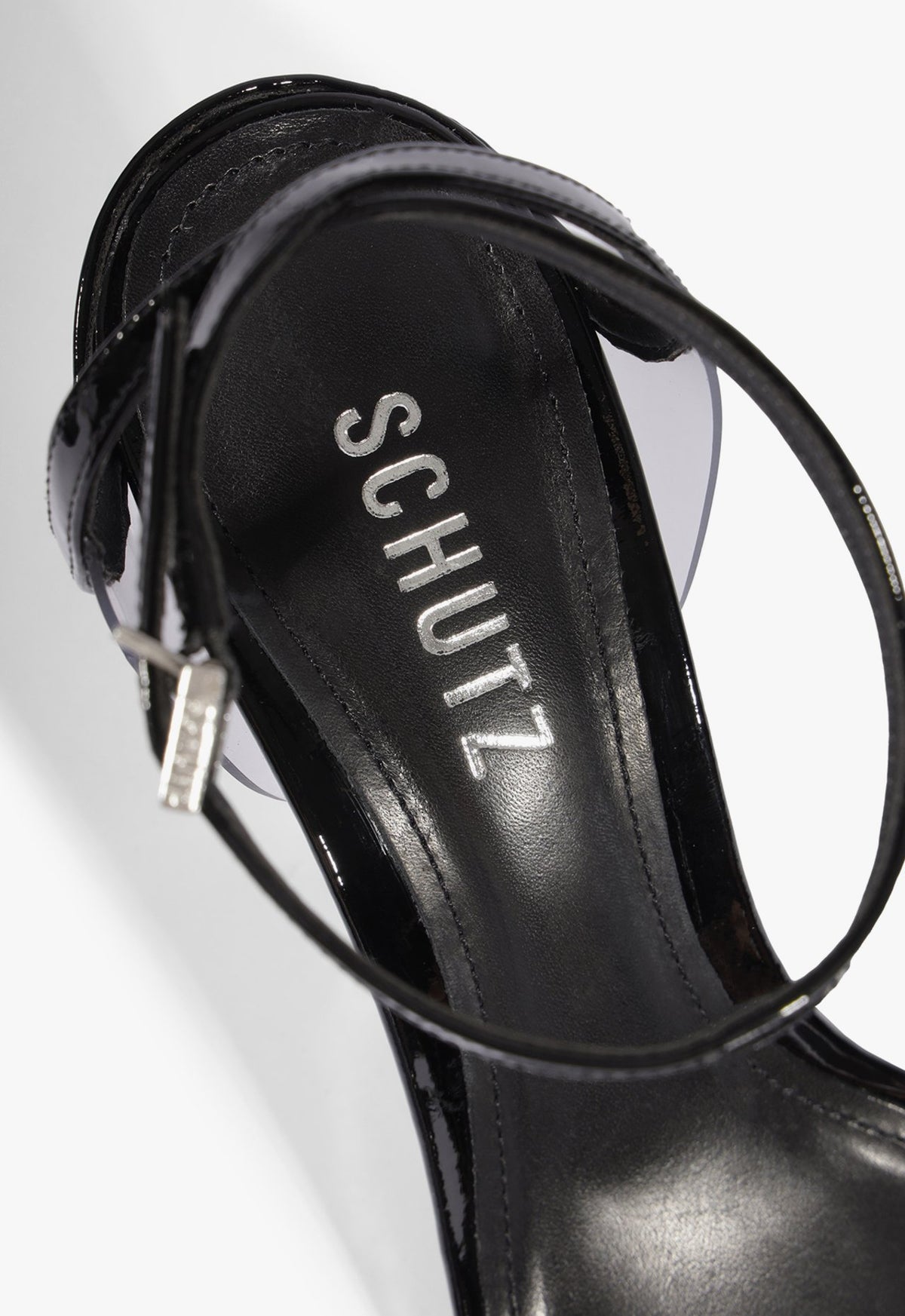 Detalhe da palmilha preta com logo Schutz e da fivela prateada na tira do tornozelo da sandália