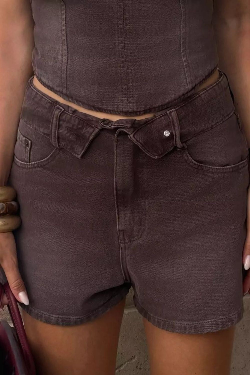 Short jeans baggy Overlap Alcance marrom, detalhe do cós com laço e botão, em close na cintura Imagem principal do produto