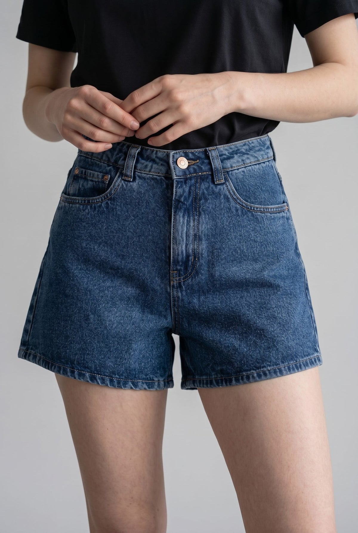 Shorts jeans Thor Lerrux em azul médio, com cintura alta, botão e zíper, vestidos com camiseta preta
